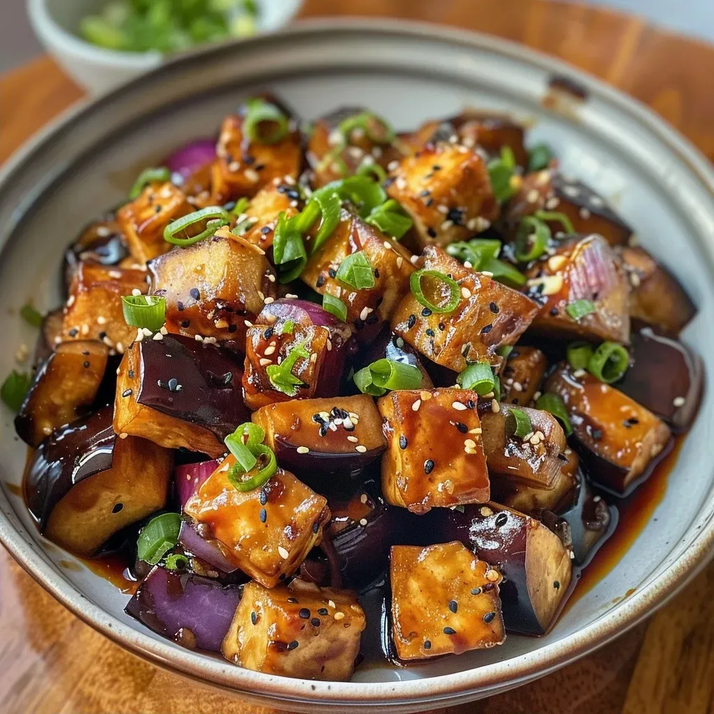 Side view of a mouthwatering crispy tofu and aubergine dish garnished with spring onions and sesame seeds.