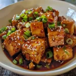 Close-up of crispy tofu with a golden-brown exterior and garnished with green onions and sesame seeds.