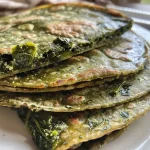 Freshly made spinach tortillas stacked on a wooden surface.