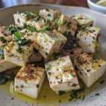Close-up of crispy tofu cubes garnished with herbs and lemon.