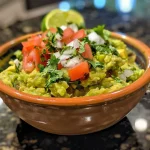 A close-up view of creamy guacamole in a bowl, with diced tomatoes and cilantro.